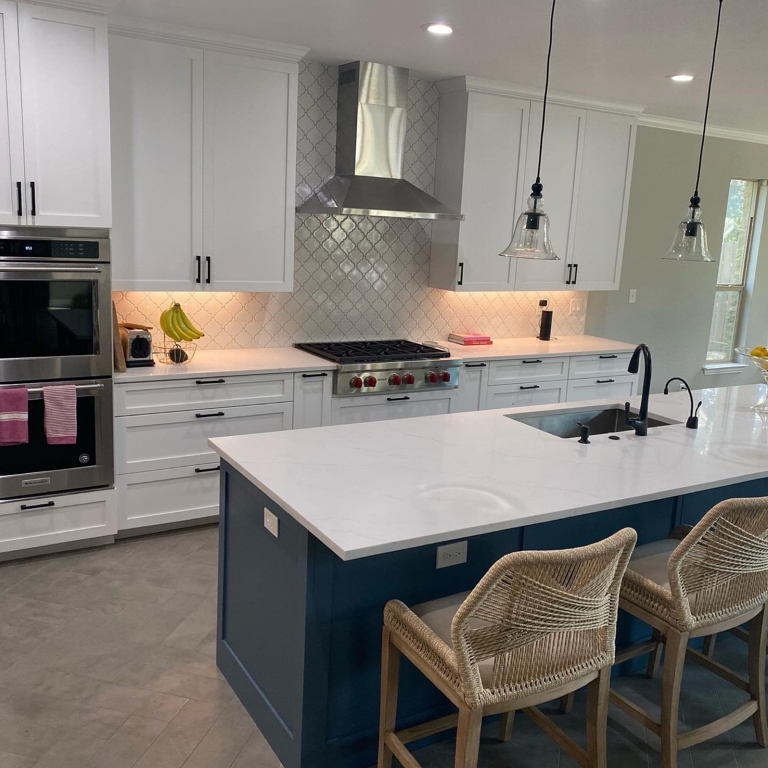 White shaker kitchen with a navy blue island, quartz countertops, and woven counter stools in Georgetown, TX